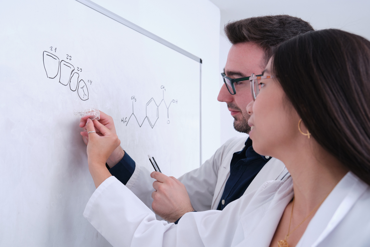 Two dentist students learning dental anatomy on a whiteboard. Two dentist students learning dental anatomy with invisible braces aligner writing on a whiteboard.