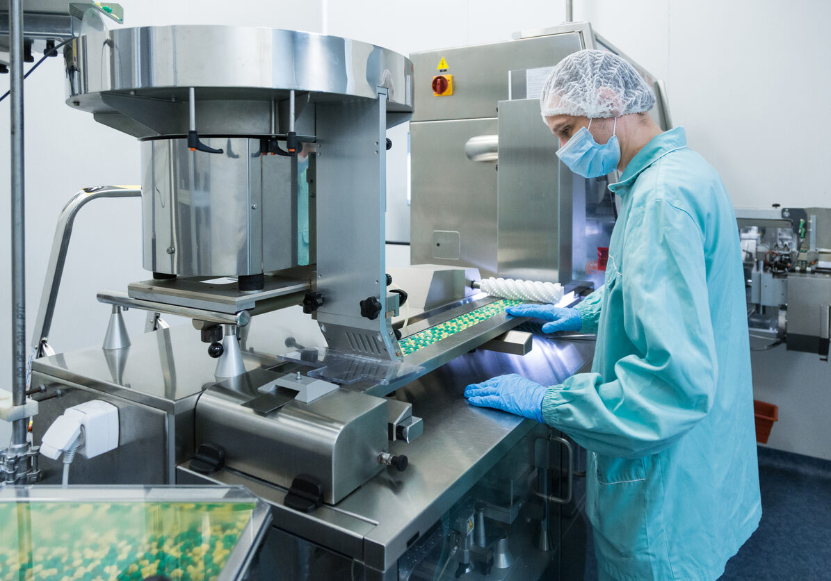 Pharmaceutical industry man worker in protective clothing operating production of tablets in sterile working conditions Pharmaceutical technician in sterile environment working on production of pills at pharmacy factory