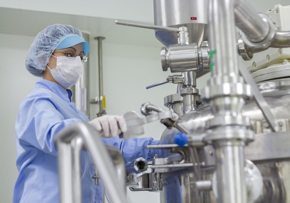 Portrait of Pharmaceutical Worker - Sterile Environment Preparing machine for work in pharmaceutical factory. Female worker wearing protective clothing in pharmaceutical plant.